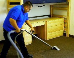 A man in a blue shirt cleaning carpet with vacuum.