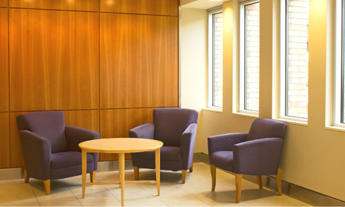 Office sitting area with wooden paneling and 3 grey chairs.