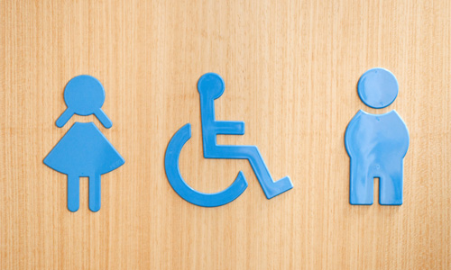 3 blue restroom symbols: women; handicapped; men, all on a wooden background.