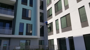 man rappelling from a building and power washing a windowsill